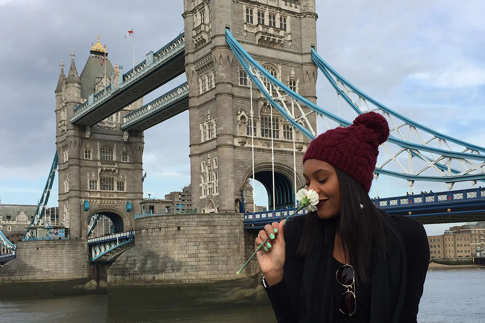 Female USC Annenberg student smelling a white flower in front of London Bridge, representing the Dual Degree in Global Communication program at USC Annenberg School