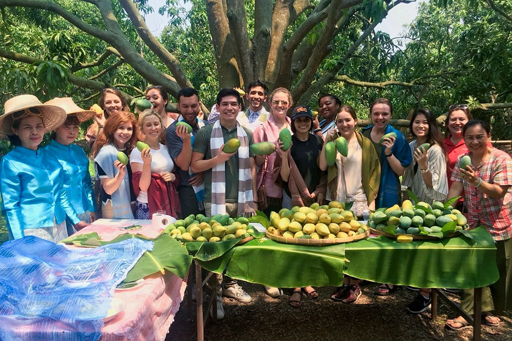 Group of people at USC Annenberg East Asian Studies Center event examining fresh mangoes on a table outdoors.