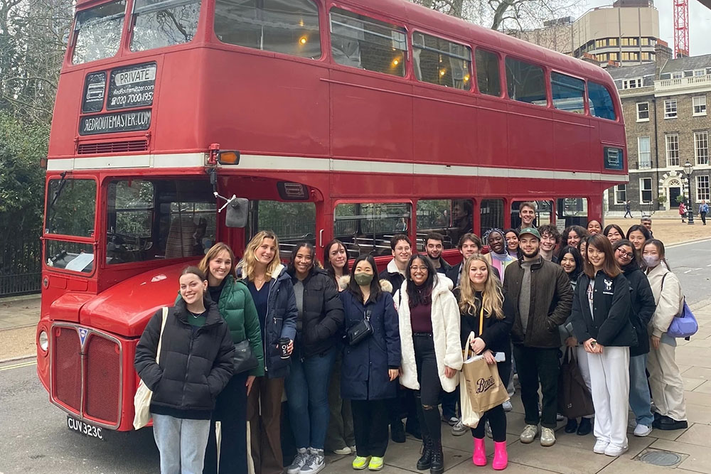 USC students on an international trip standing in front of a red double-decker bus, representing the university’s commitment to safe and healthy travel experiences through partnerships with International SOS