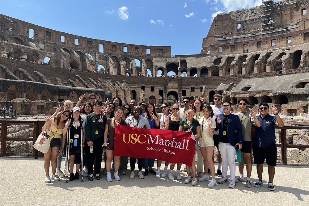 Students from USC Marshall School of Business holding a banner at the Colosseum in Rome, representing the World Bachelor of Business partnership with Bocconi University and Hong Kong University of Science and Technology.